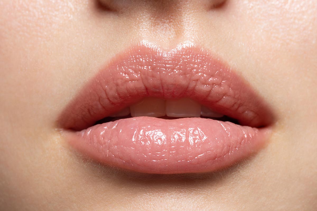 Close up of young woman wearing light fresh lip make up and slightly opening mouth. Plump lips with natural makeup. Part of female face