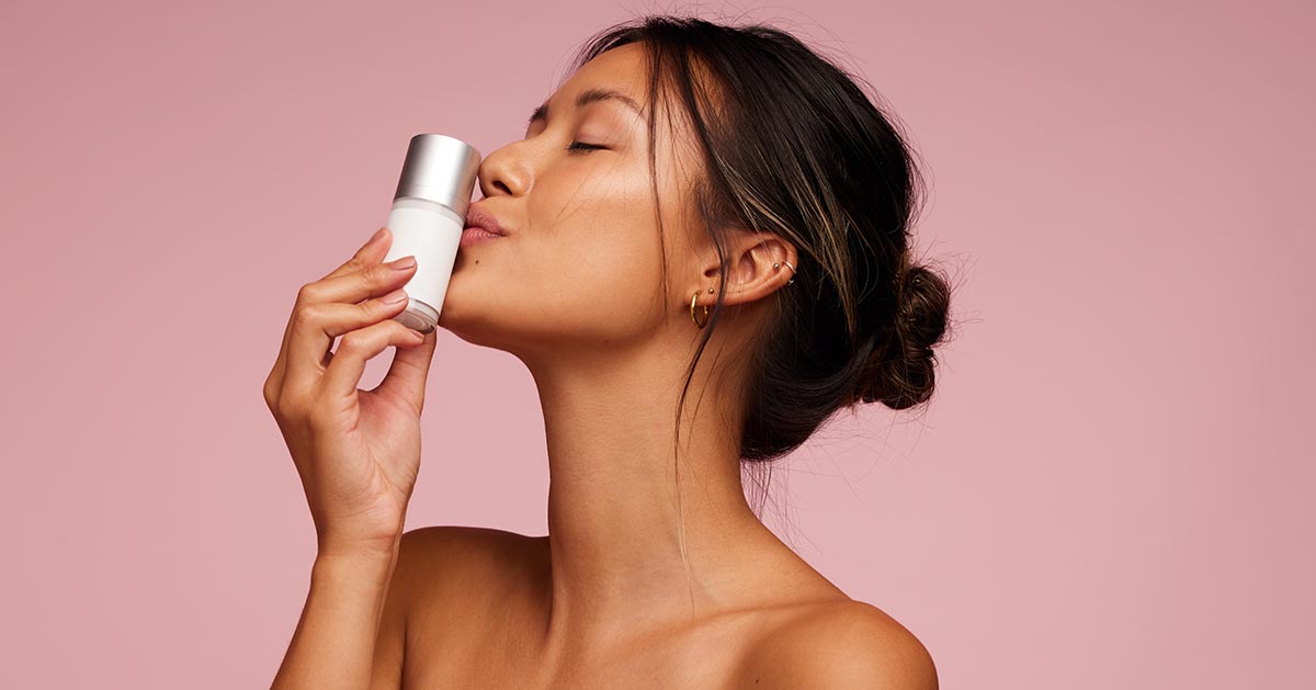 Attractive asian woman kissing a skincare product bottle. Female with best cosmetic product for skin.