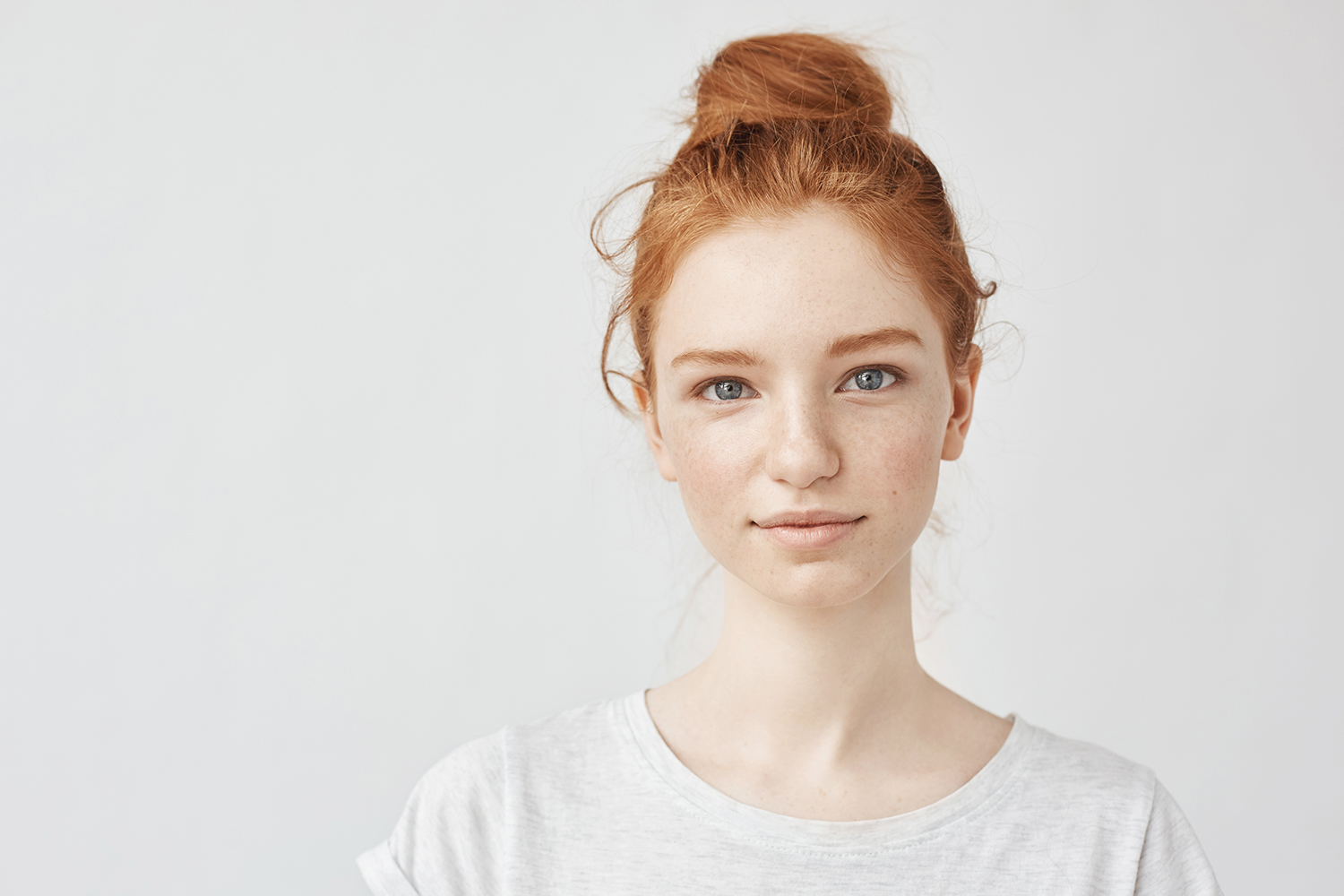 Portrait of young beautiful redhead girl smiling looking at camera. Copy space. Isolated on white background.